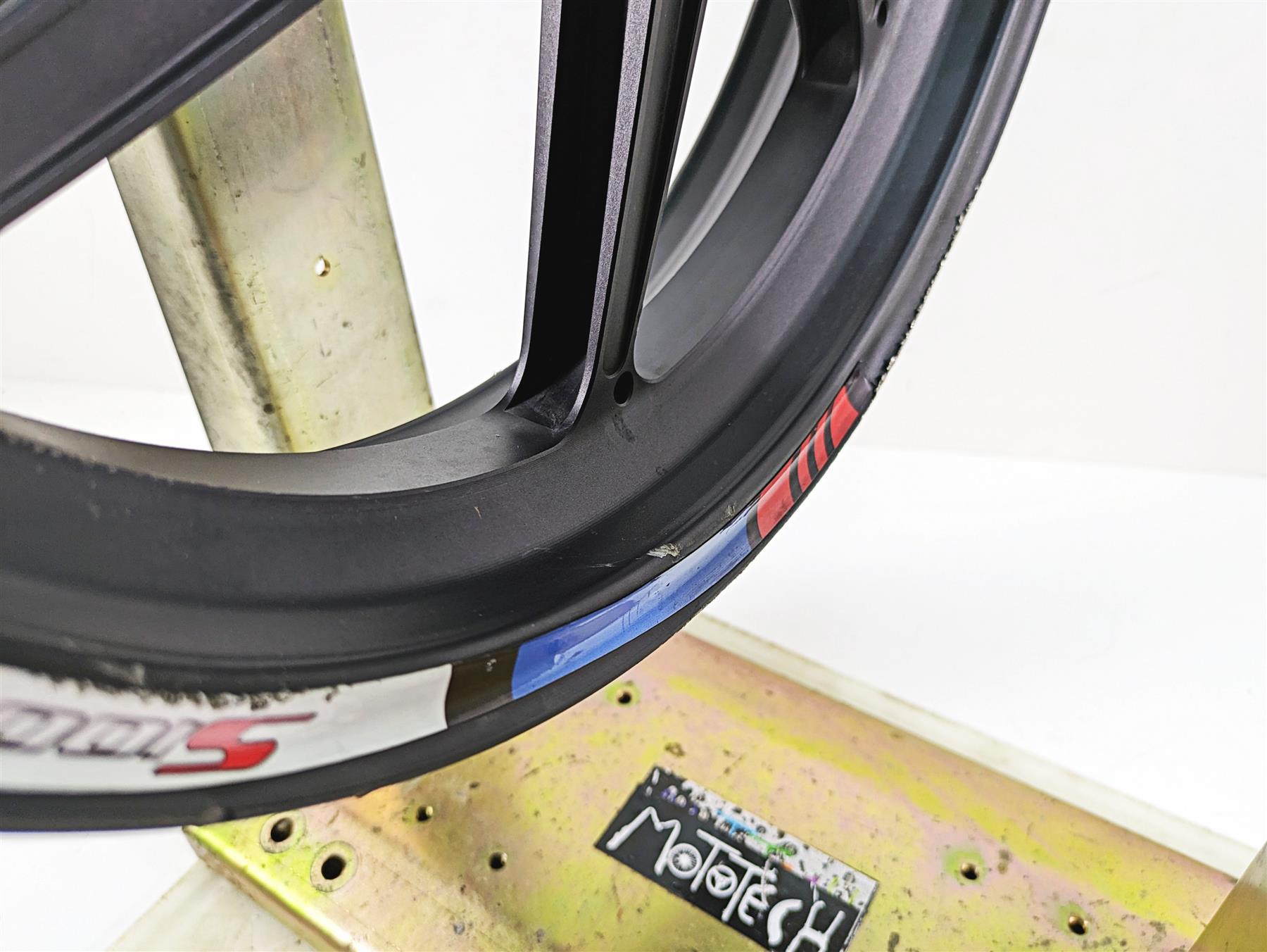 Close-up of a used black motorcycle wheel rim with decals and minor wear, available at Mototech271