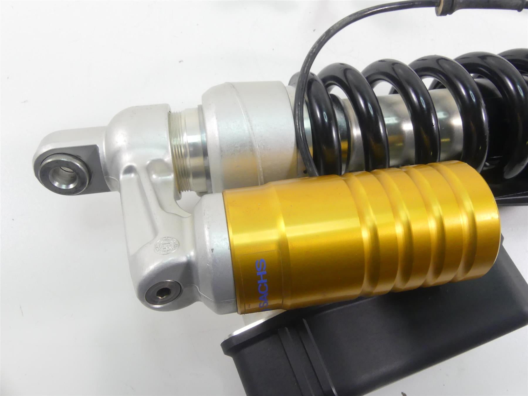 Close-up of a motorcycle rear shock absorber with gold reservoir, available at Mototech271