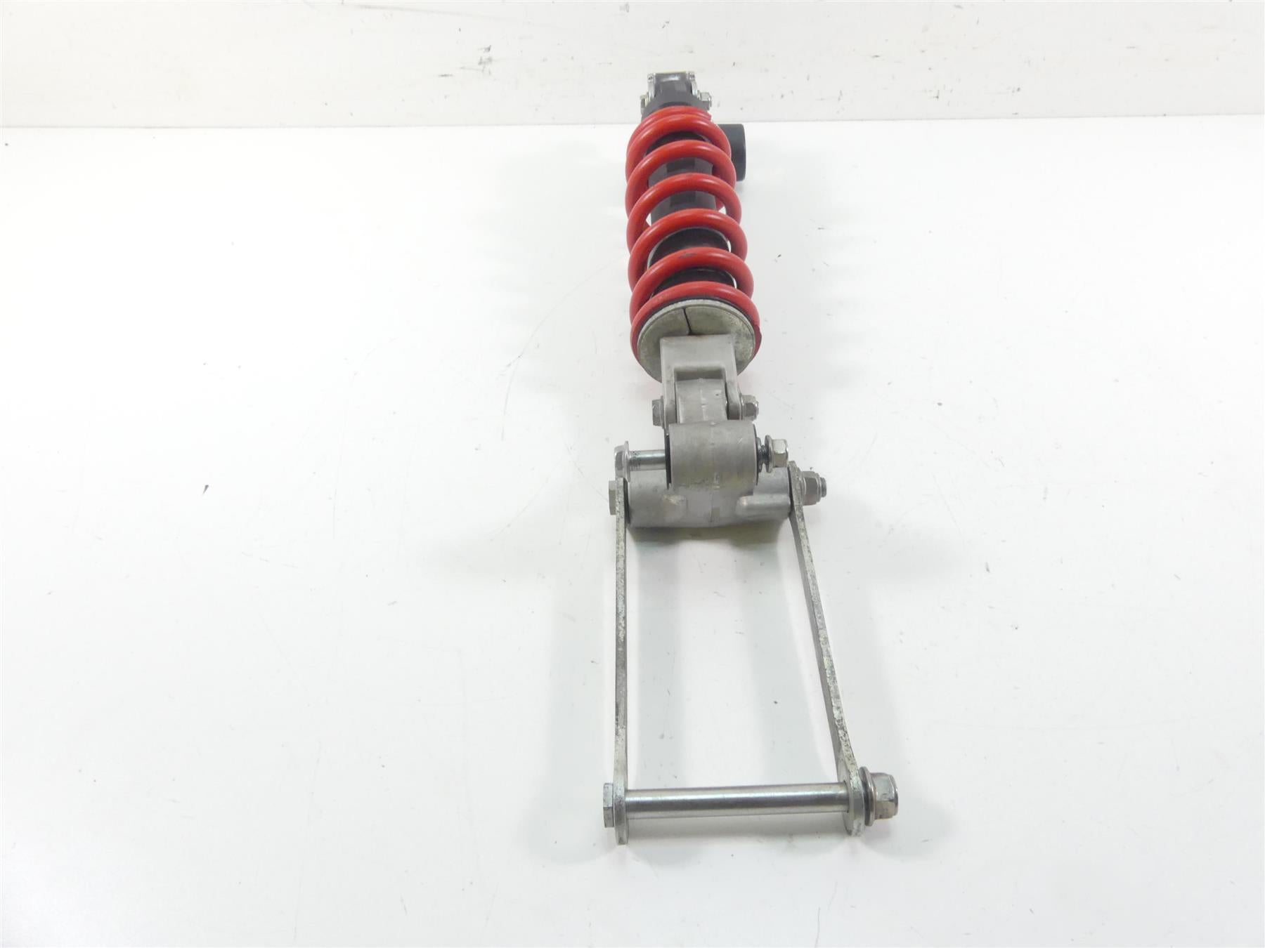 Used motorcycle rear shock absorber with red coil spring and linkage on white background, available at Mototech271