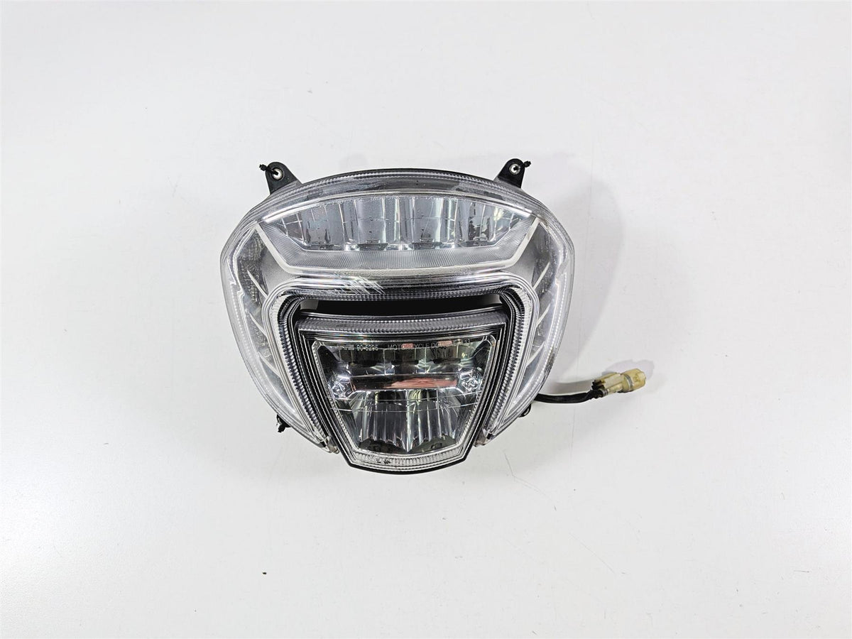 Used motorcycle headlight assembly with clear lens and wiring harness on white background