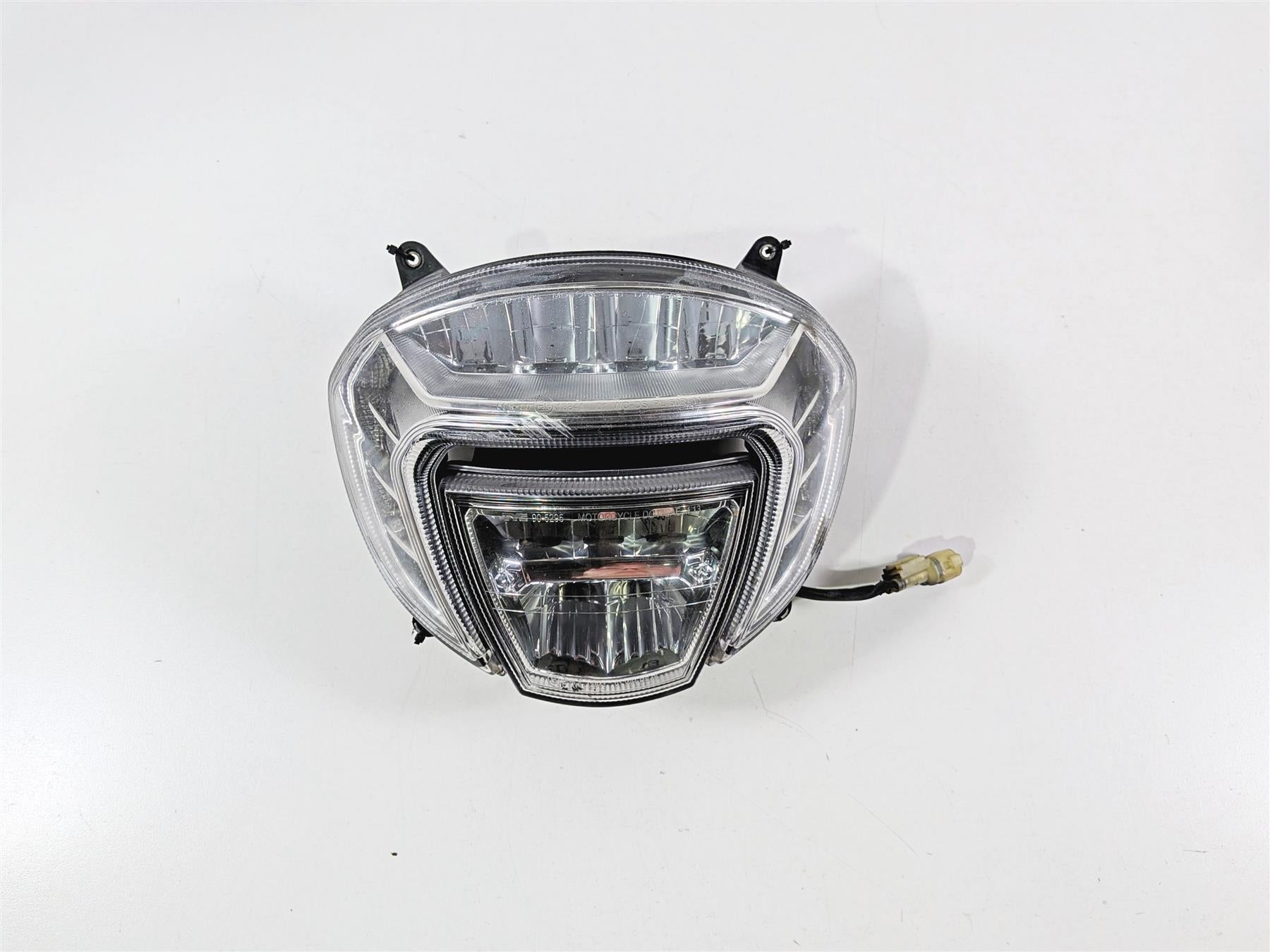 Used motorcycle headlight assembly with clear lens and wiring harness on white background