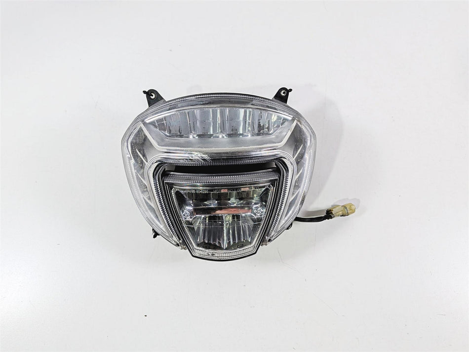 Used motorcycle headlight assembly with clear lens and wiring harness on white background