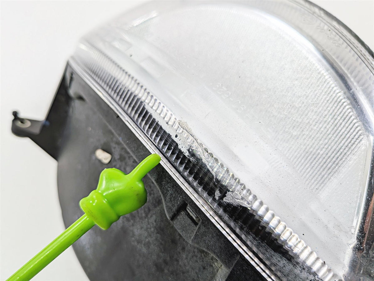 Close-up of used motorcycle headlight with scratch on lens, green pointer indicating damage