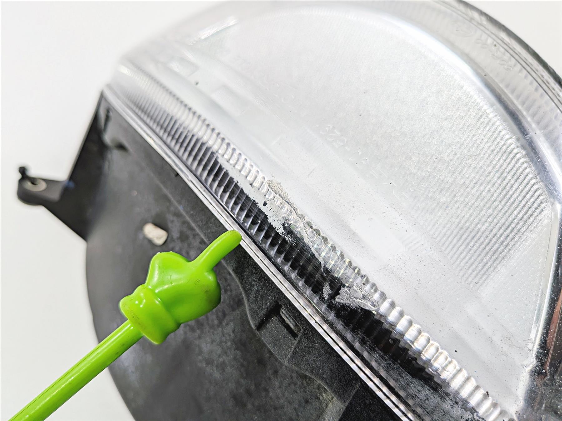 Close-up of used motorcycle headlight with scratch on lens, green pointer indicating damage