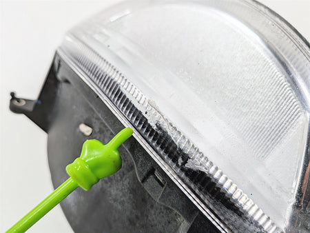 Close-up of used motorcycle headlight with scratch on lens, green pointer indicating damage