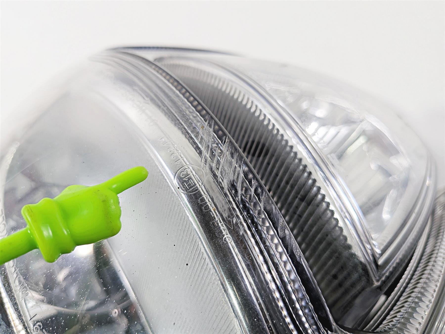 Close-up of used motorcycle headlight lens with green pointer indicating detail