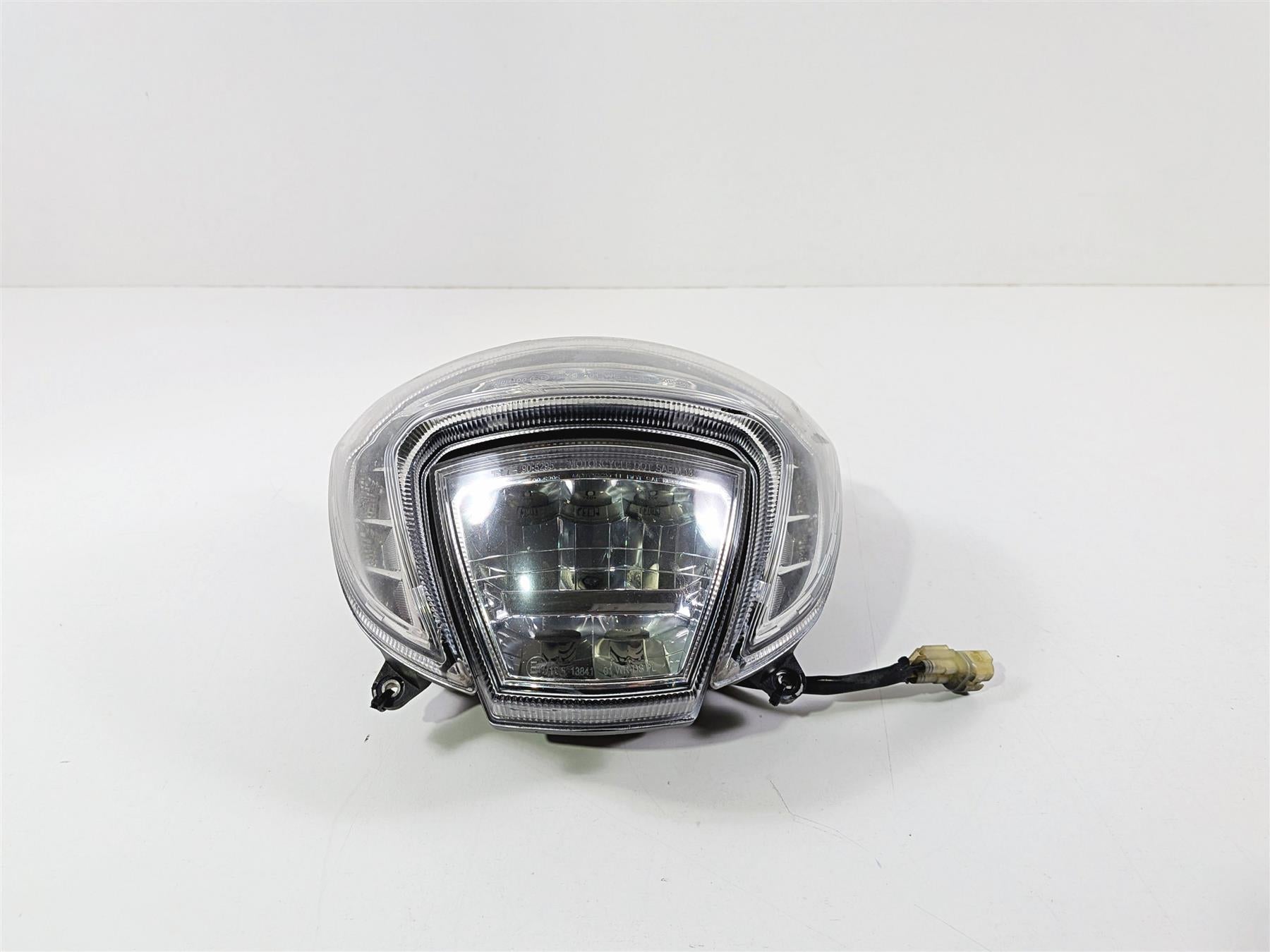 Used motorcycle headlight assembly with clear lens and wiring harness on white background